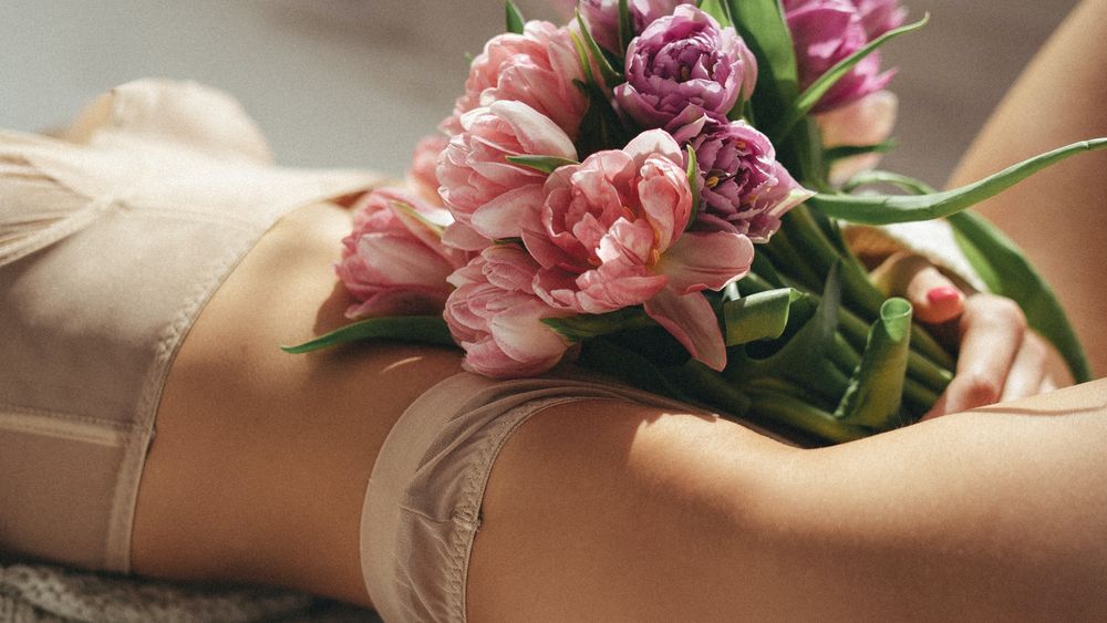 Une femme en ligerie couleur peau avec un bouquet de fleur